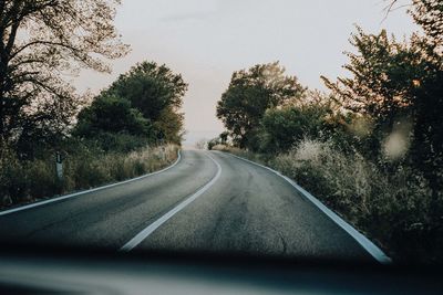 Road amidst trees against sky seen through car windshield