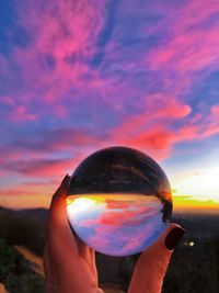 Midsection of person holding crystal ball against sky during sunset