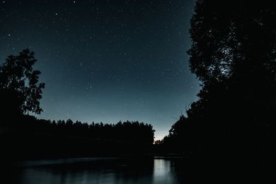 Silhouette trees by lake against sky at night