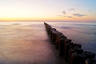Wooden posts in sea against sky during sunset