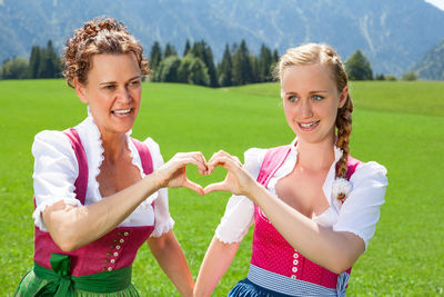 Portrait of happy young woman making heart shape while standing on field