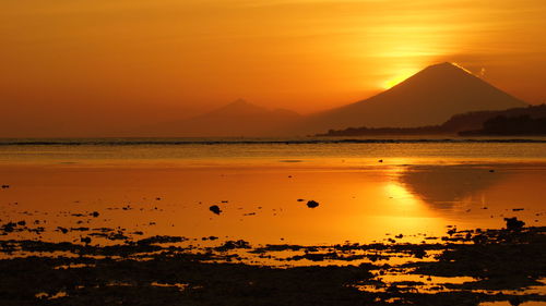 Scenic view of lake and mountains against orange sky during sunset