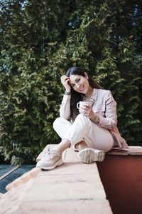 Young woman using mobile phone while sitting on tree