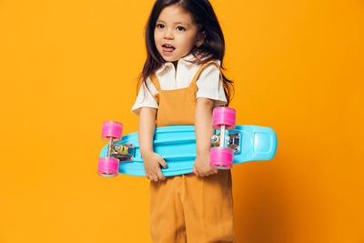 Portrait of young woman holding gift box against yellow background