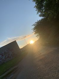 Road by trees against sky during sunset