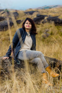 Young woman looking away while sitting on field against sky