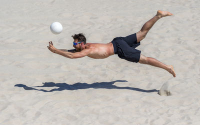 Shirtless man playing volleyball at beach