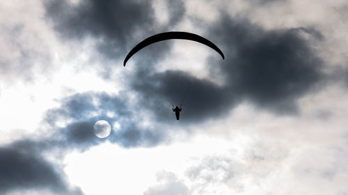 Low angle view of silhouette person paragliding against sky