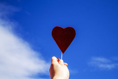 Cropped hand of person holding heart shape candy against sky