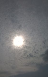 Low angle view of sun shining through clouds in sky