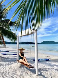 Woman sitting on beach by sea against sky