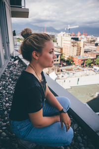 Young woman sitting in car against sky in city