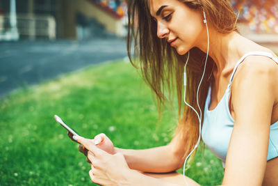 Young woman listening to music while sitting on field