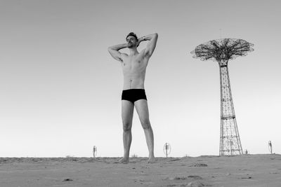 Shirtless man standing at beach against sky