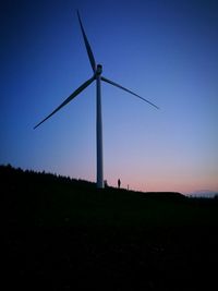 Silhouette of wind turbines on field against clear sky