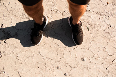 From above of crop faceless male athlete in stylish black sneakers and shorts standing on arid ground after training in countryside