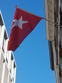 Low angle view of flag against buildings against clear blue sky