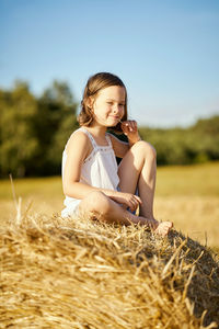 Cute little girl sits on mown rye in the field in summer