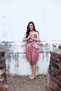 Portrait of smiling young woman standing against wall