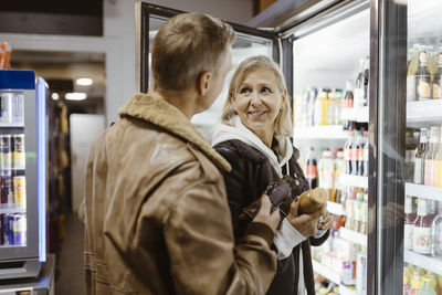 Smiling woman looking at man while buying beverages from refrigerated section at supermarket