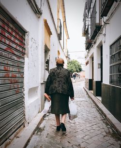 Rear view of woman walking on footpath amidst buildings