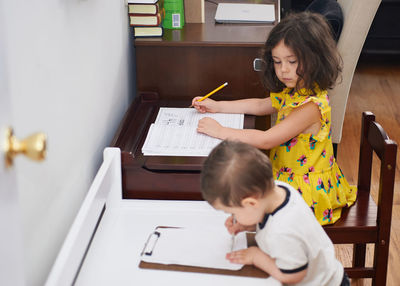 Little toddler copying his sister doing her homework