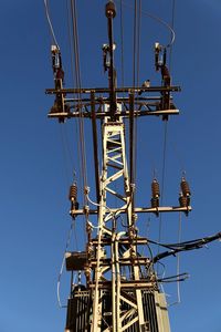 Low angle view of electricity pylon against clear blue sky