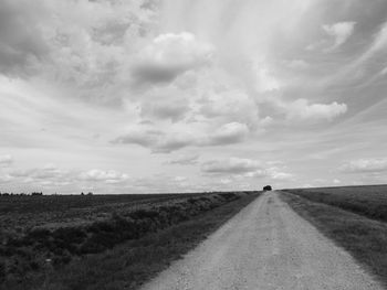 Dirt road amidst field against sky