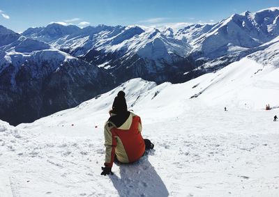 Rear view of person sitting on snowcapped mountain during sunny day