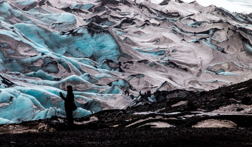 Side view of man standing on field against snowcapped mountains