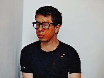 Close-up of man wearing eyeglasses against white wall