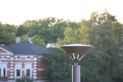 Close-up of electric lamp against trees and building