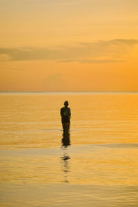 Silhouette man standing in sea against orange sky