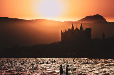 Silhouette people in river against mountains during sunset