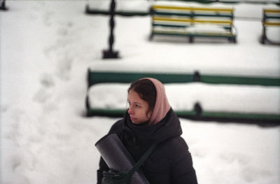 Young woman looking away while standing outdoors during winter