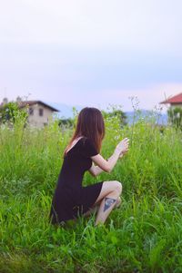 Woman crouching on field against sky