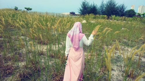 Rear view of woman walking amidst grass on field