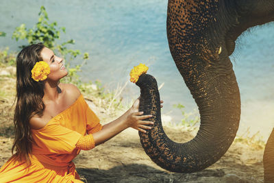 Smiling woman with flower touching elephant trunk