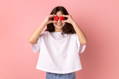 Woman holding heart shape against pink background