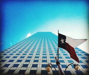 Low angle view of flag against building against blue sky