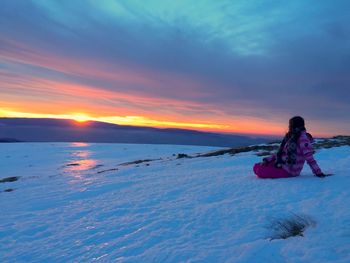 Woman sitting on shore against sea during sunset