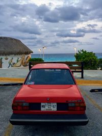 Red car on road by city against sky