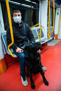 Full body of male passenger in medical mask riding in metro train with guide dog