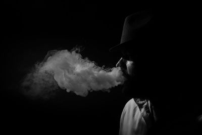 Side view of young man smoking against black background