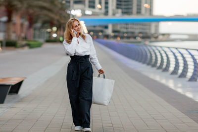 Young woman at the street with shopping bags talking on mobile phone