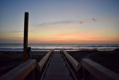 Wooden benches on beach against sky during sunset