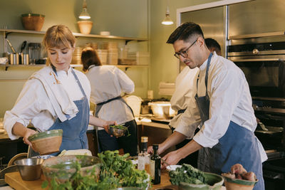 Male and female chef helping each other while preparing food in commercial kitchen