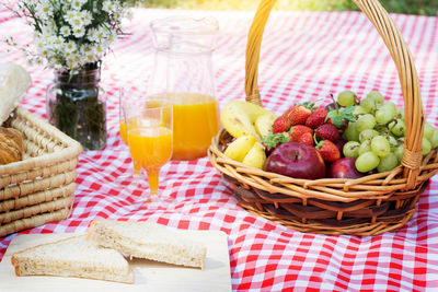 Close-up of fruits in basket by orange juice on picnic blanket