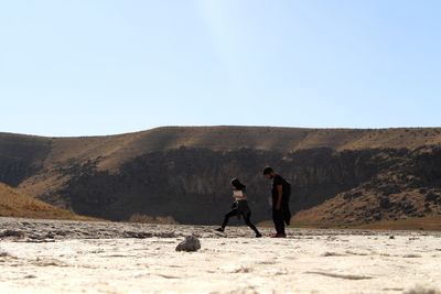 People walking on field against clear sky during sunny day