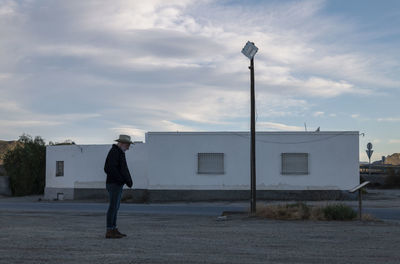 Adult man in cowboy hat standing in front of white building against sky